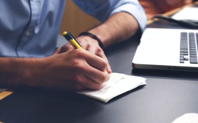 Man with computer taking notes on a notepad.